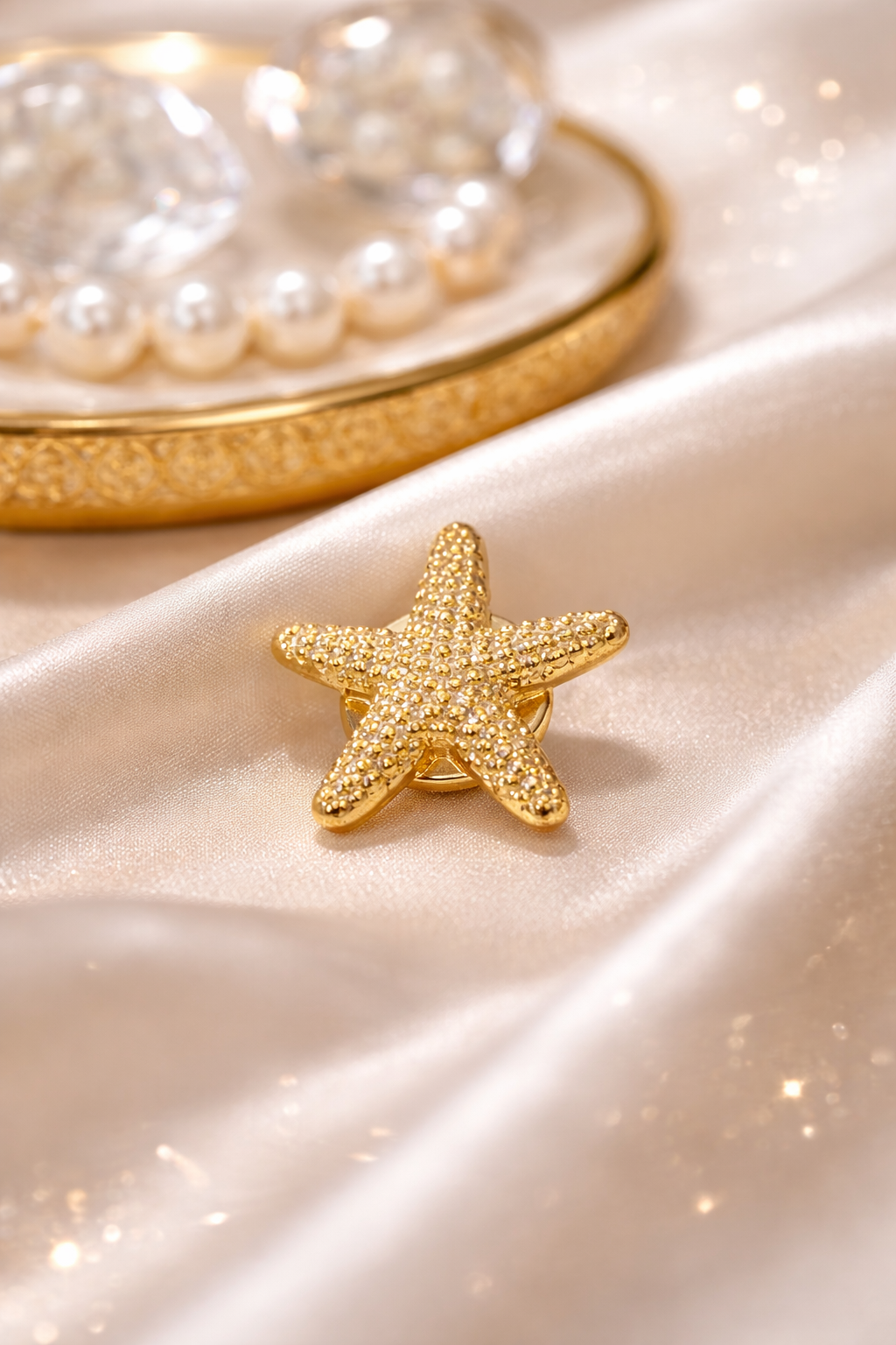 Gold starfish-shaped jewelry on a satin surface with pearls in the background