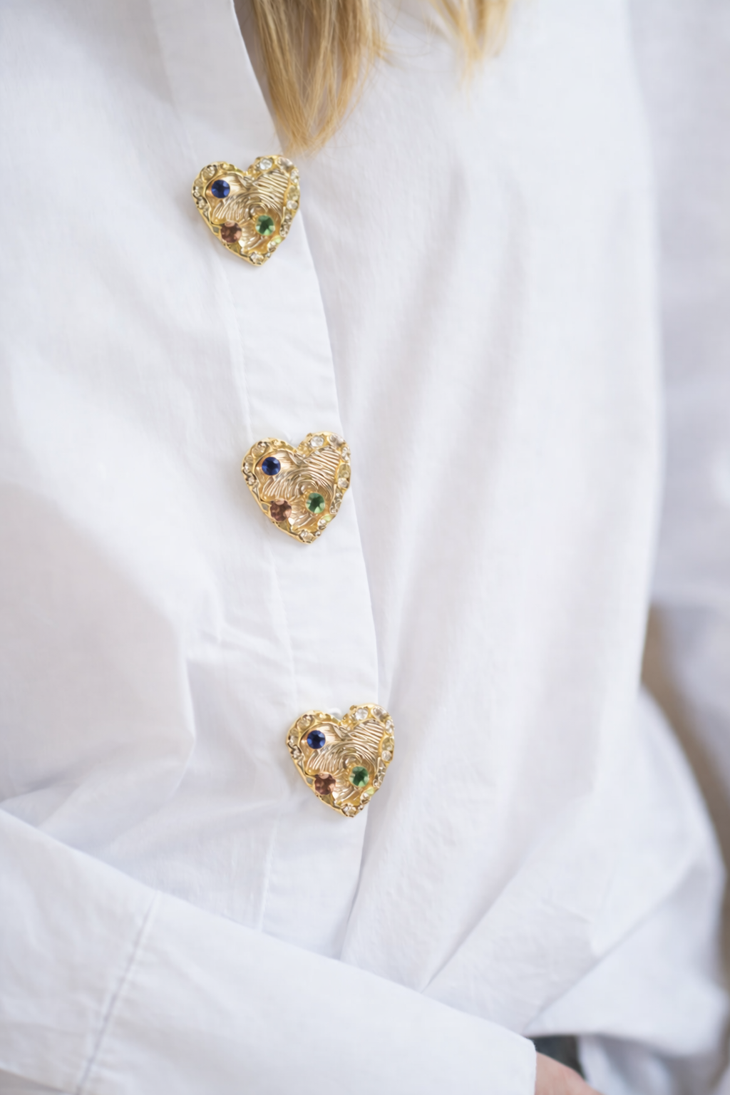 Close-up of a white coat with gold heart-shaped brooches on a blurred background
