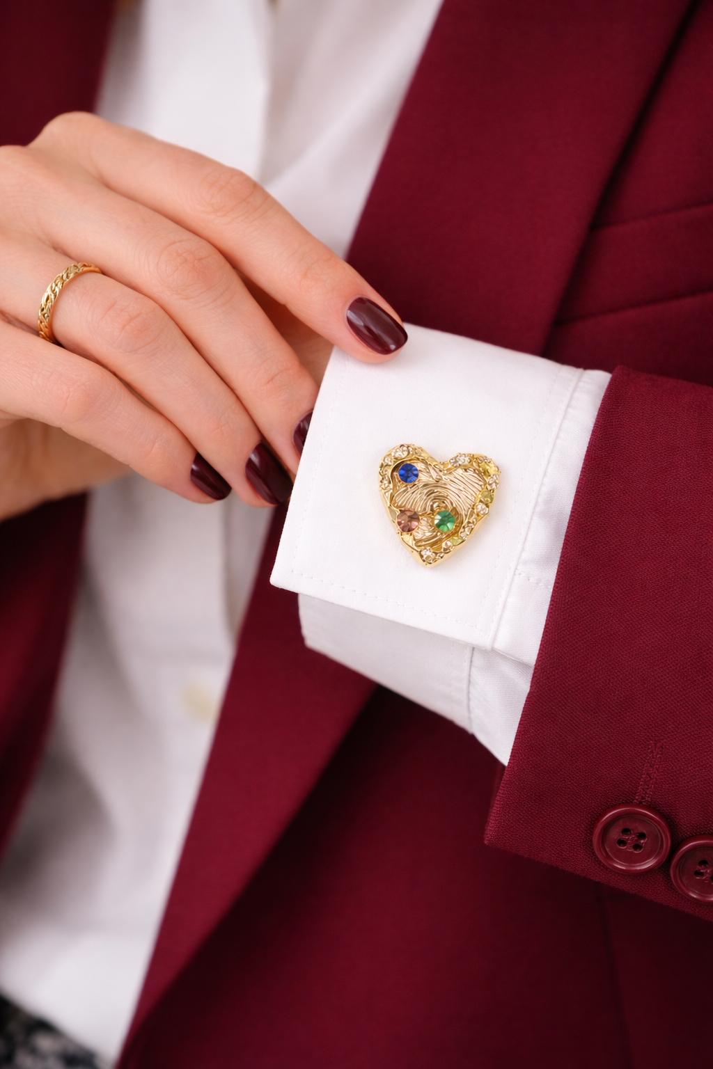 Gold heart-shaped button cover with colored stones on a white cuff against a red blazer.