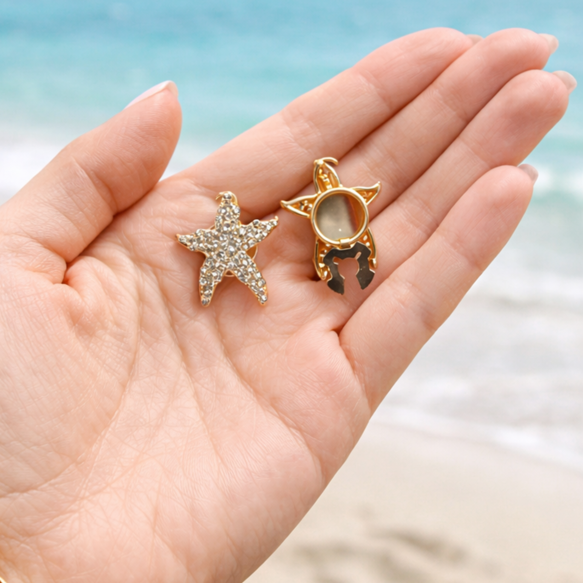 Star-shaped jewelry pieces held in a hand with a blurred beach background